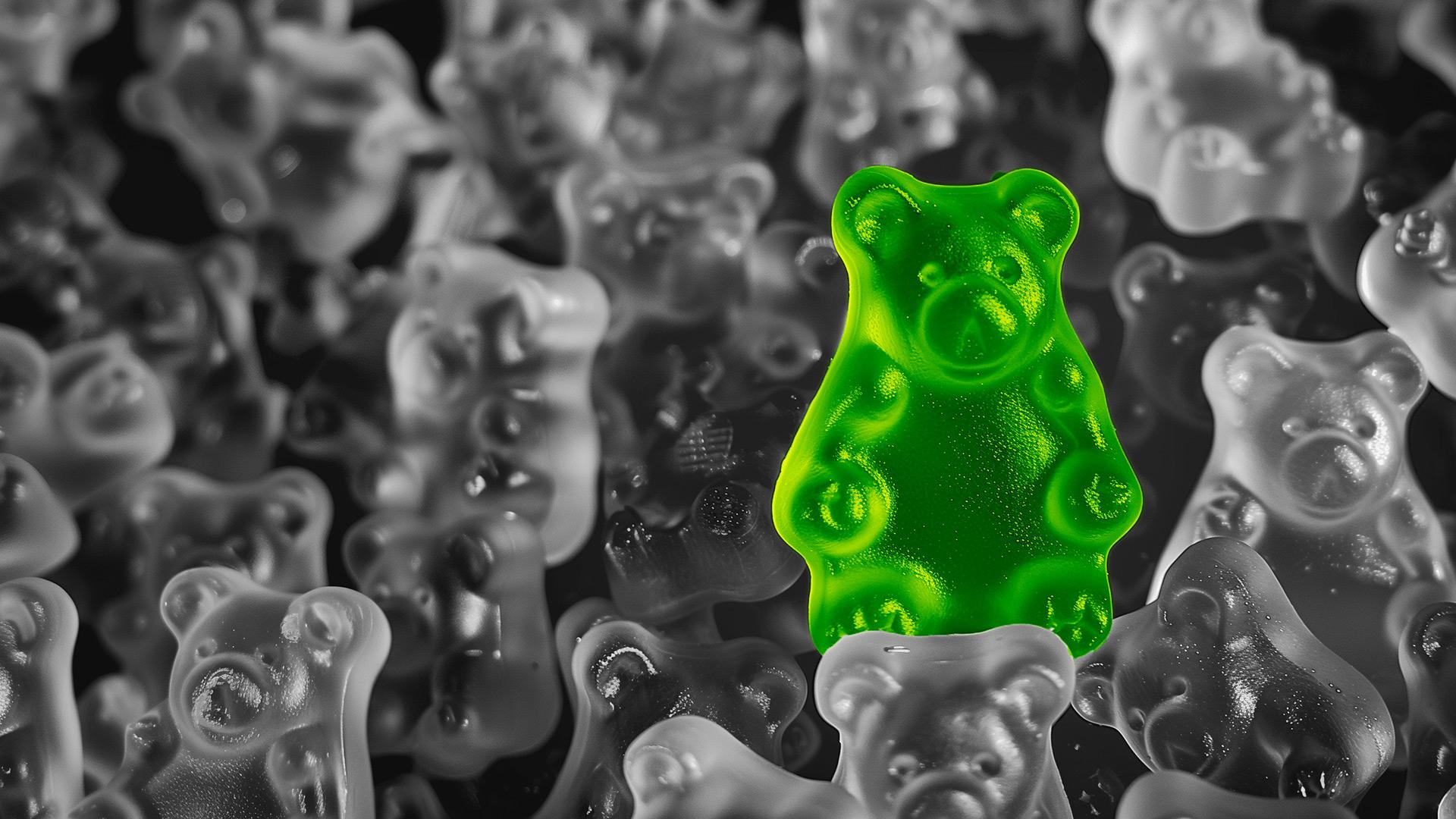ein grünes Gummibärchen umgeben von weißen Gummibärchen