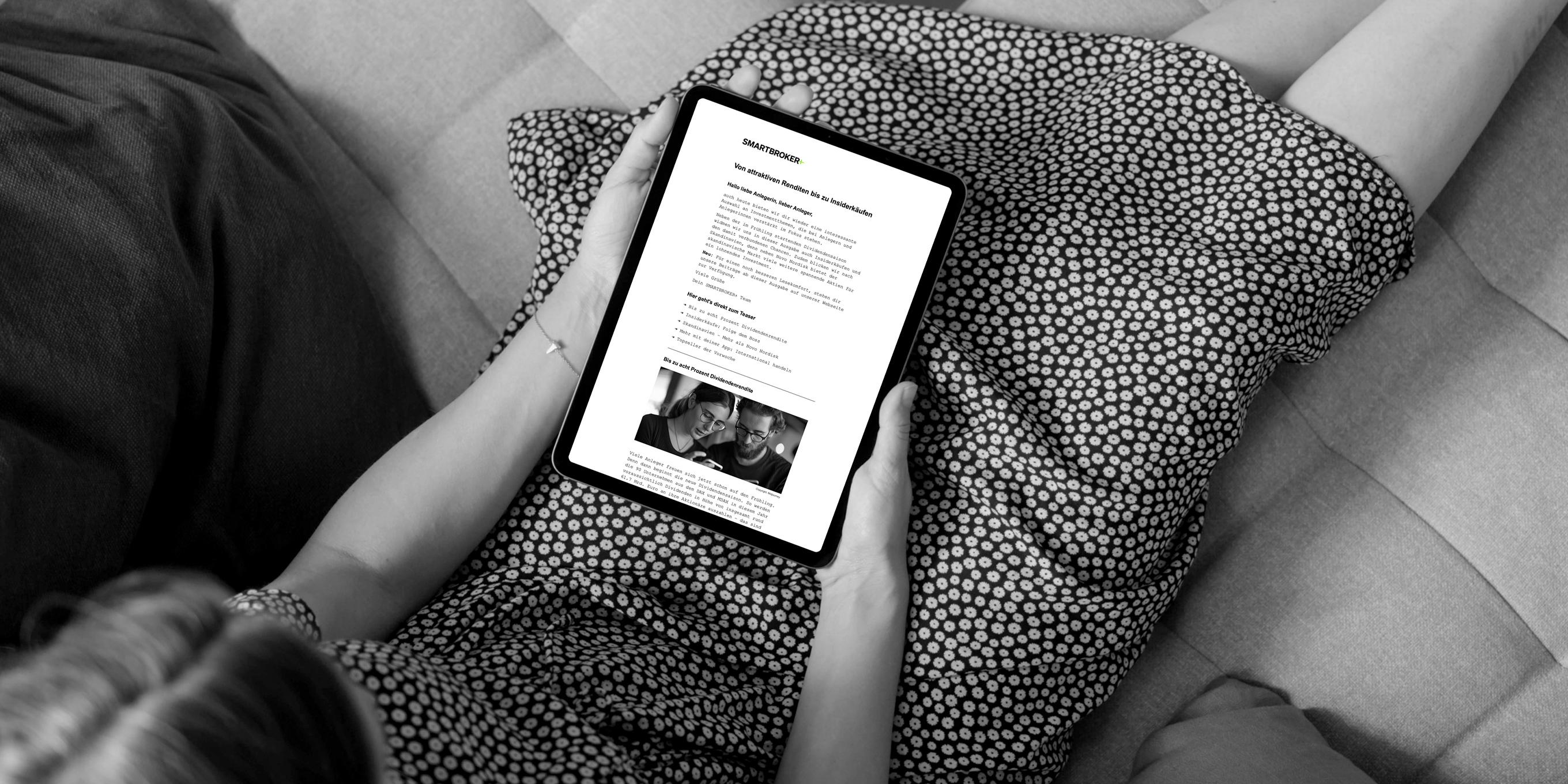 Eine Frau sitzt auf einem Sofa und liest einen Text auf einem Tablet