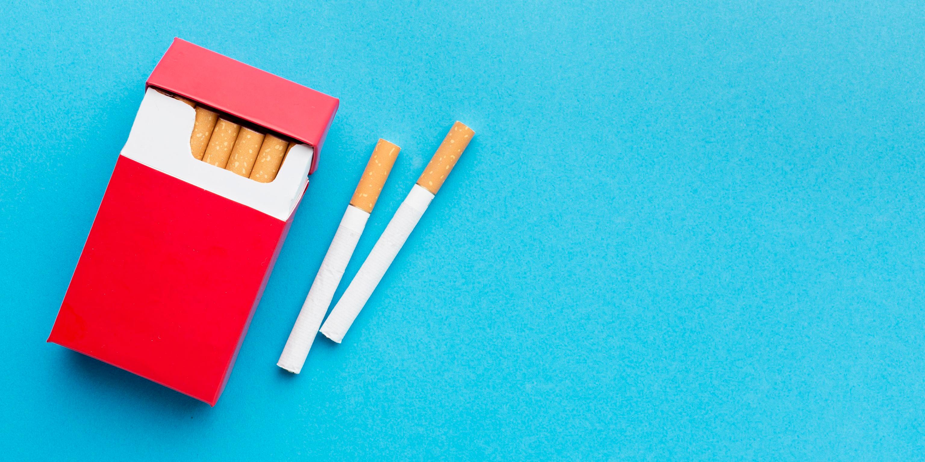 Eine Zigarettenschachtel mit zwei daneben liegenden Zigaretten